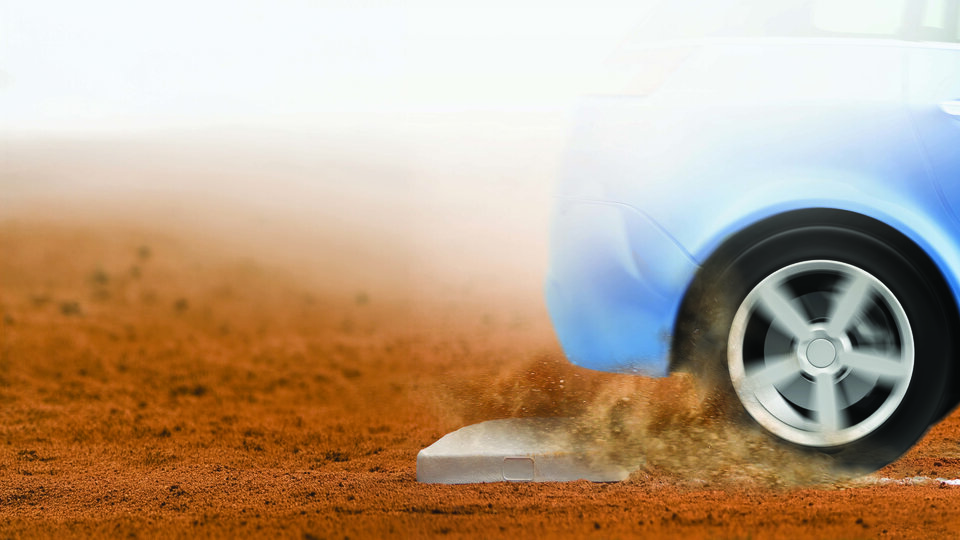 Blue car driving over a dusty terrain with rear wheel kicking up dirt.