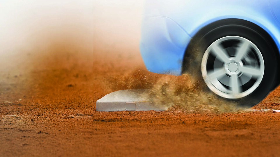 Car tire kicking up dust on a baseball field, near a base.