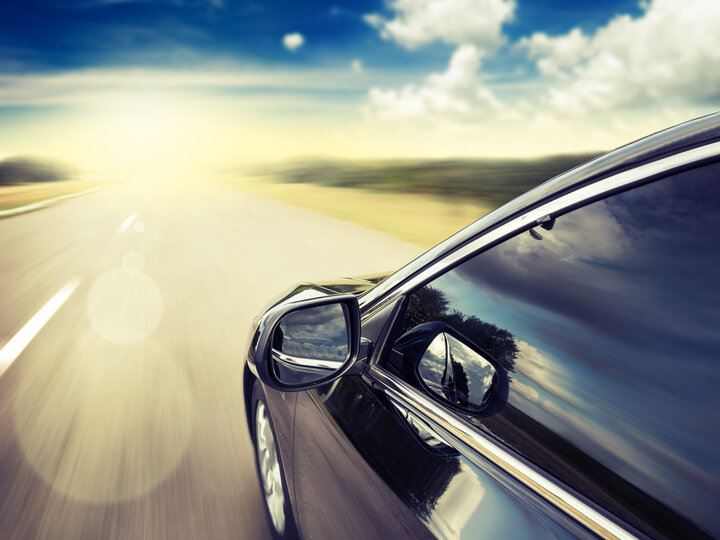 Car driving on a sunny highway, reflecting blue sky and clouds on its side.